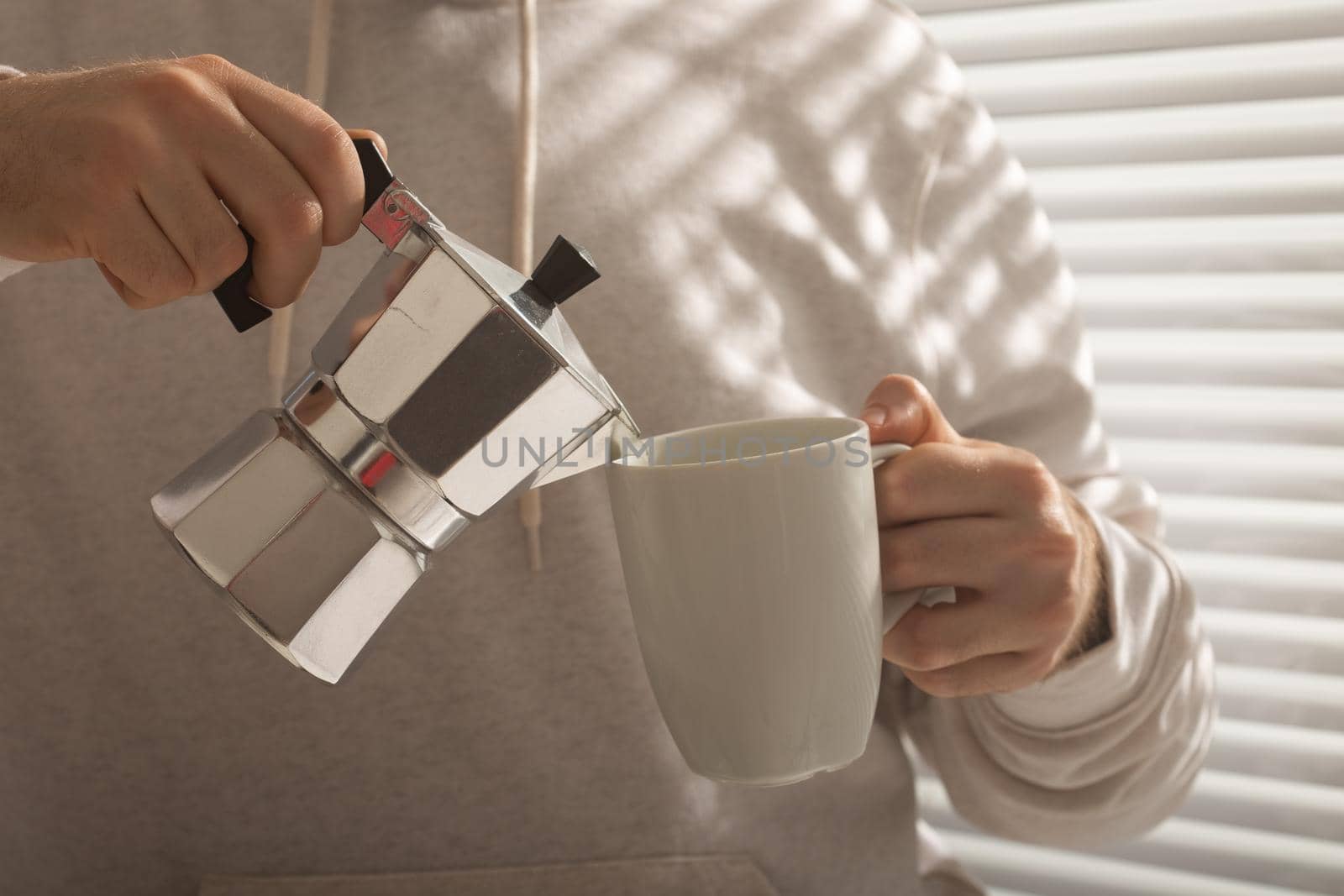 Close-up portrait of young stylish hipster male pouring coffee at office on summer day. Invigorating morning and positive mood