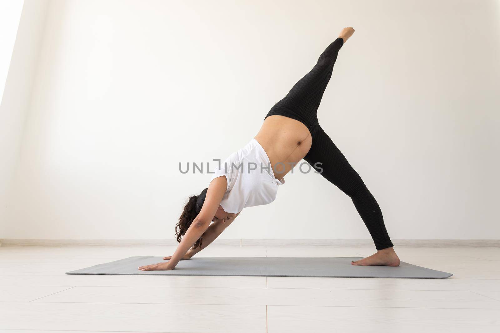 Young flexible pregnant woman doing gymnastics on rug on the floor on white background. Preparing the body for easy childbirth