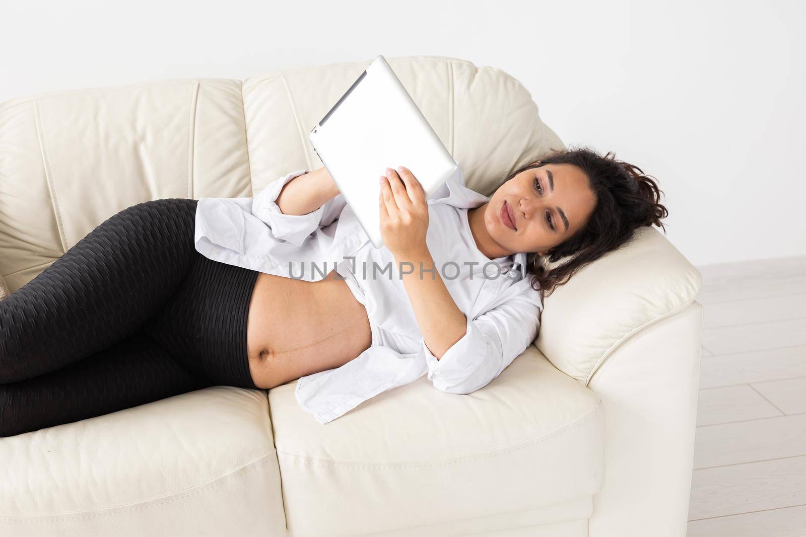Latin pregnant woman using tablet computer sitting on sofa at home. Pregnancy and information for parenthood