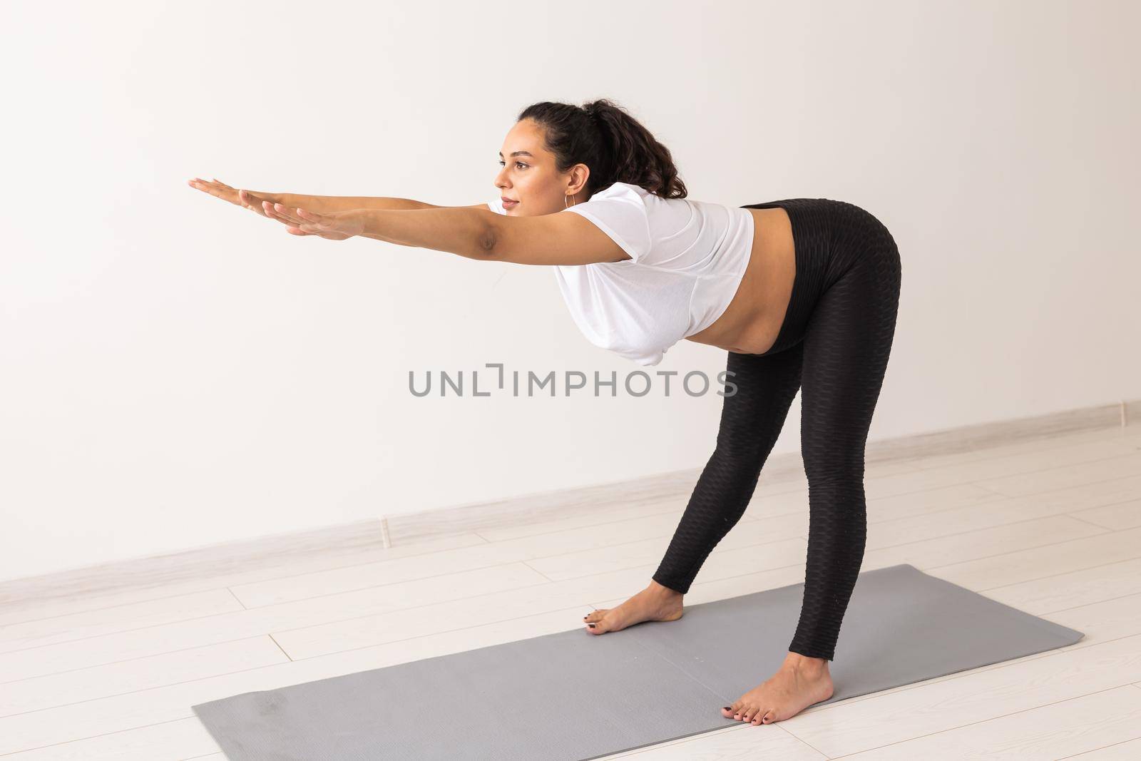 Young flexible pregnant woman doing gymnastics on rug on the floor on white background. Preparing the body for easy childbirth