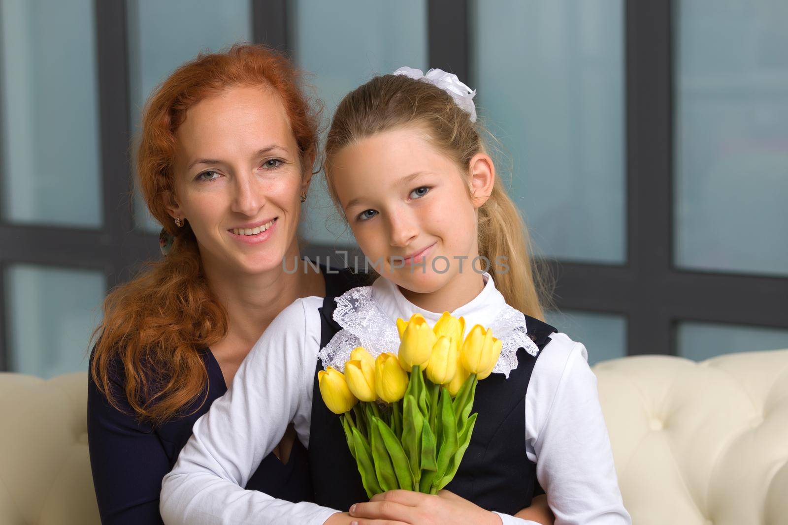 A beautiful young mother and little daughter near a bouquet of tulips, which her daughter gave to her mother for the holiday. The concept of women's holiday, family values.