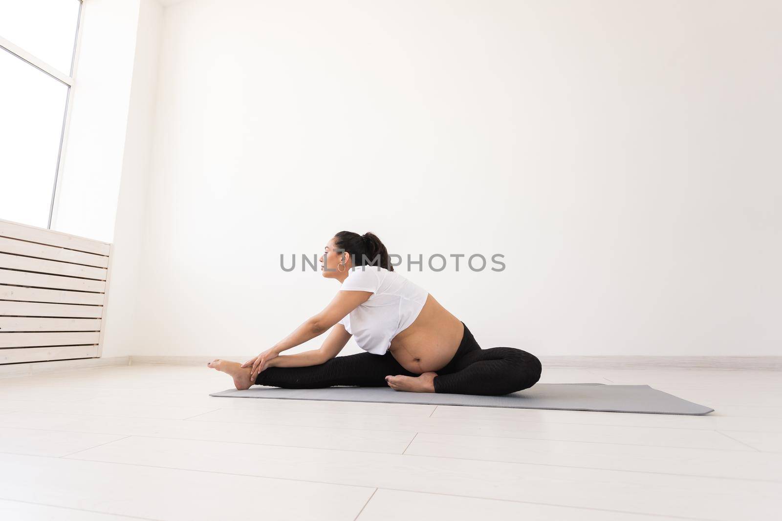 Purposeful pregnant woman exercises during yoga class and relaxes while sitting on a mat on the floor. Physical and mental preparation of the body for childbirth. Place for text