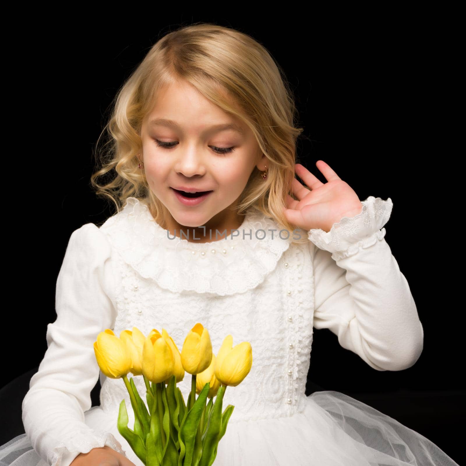 Beautiful little girl with a bouquet of tulips, studio photo on a black background. The concept of happy people, childhood.