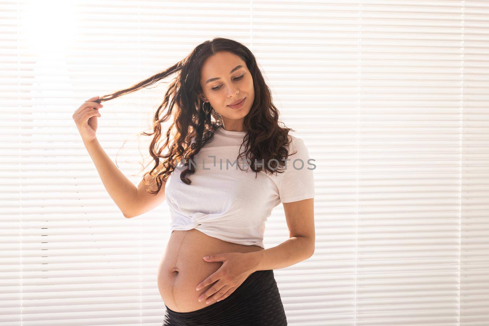 Smiling young beautiful pregnant woman touching her belly and hair and rejoicing. Health and thinking about the future while waiting for baby. Copyspace