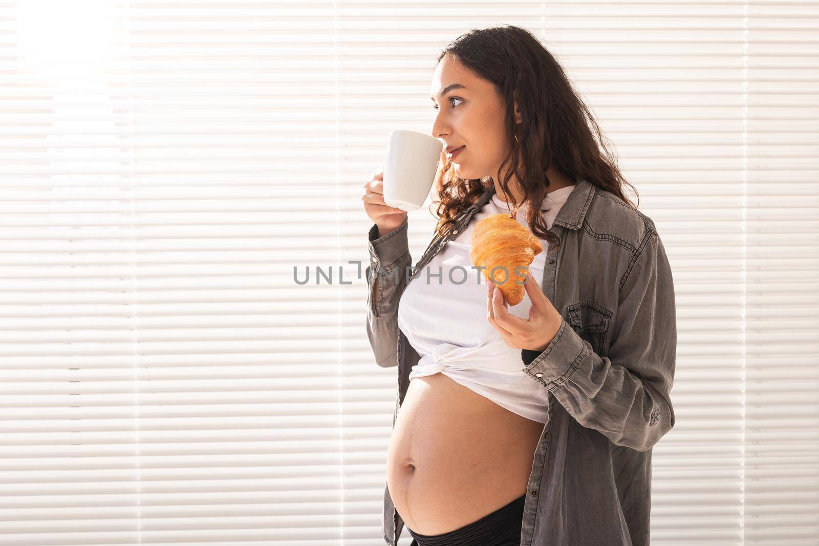 Healthy beautiful pregnant woman drinking tea and eating croissant during lunch. High-calorie nutrition while waiting for birth of baby