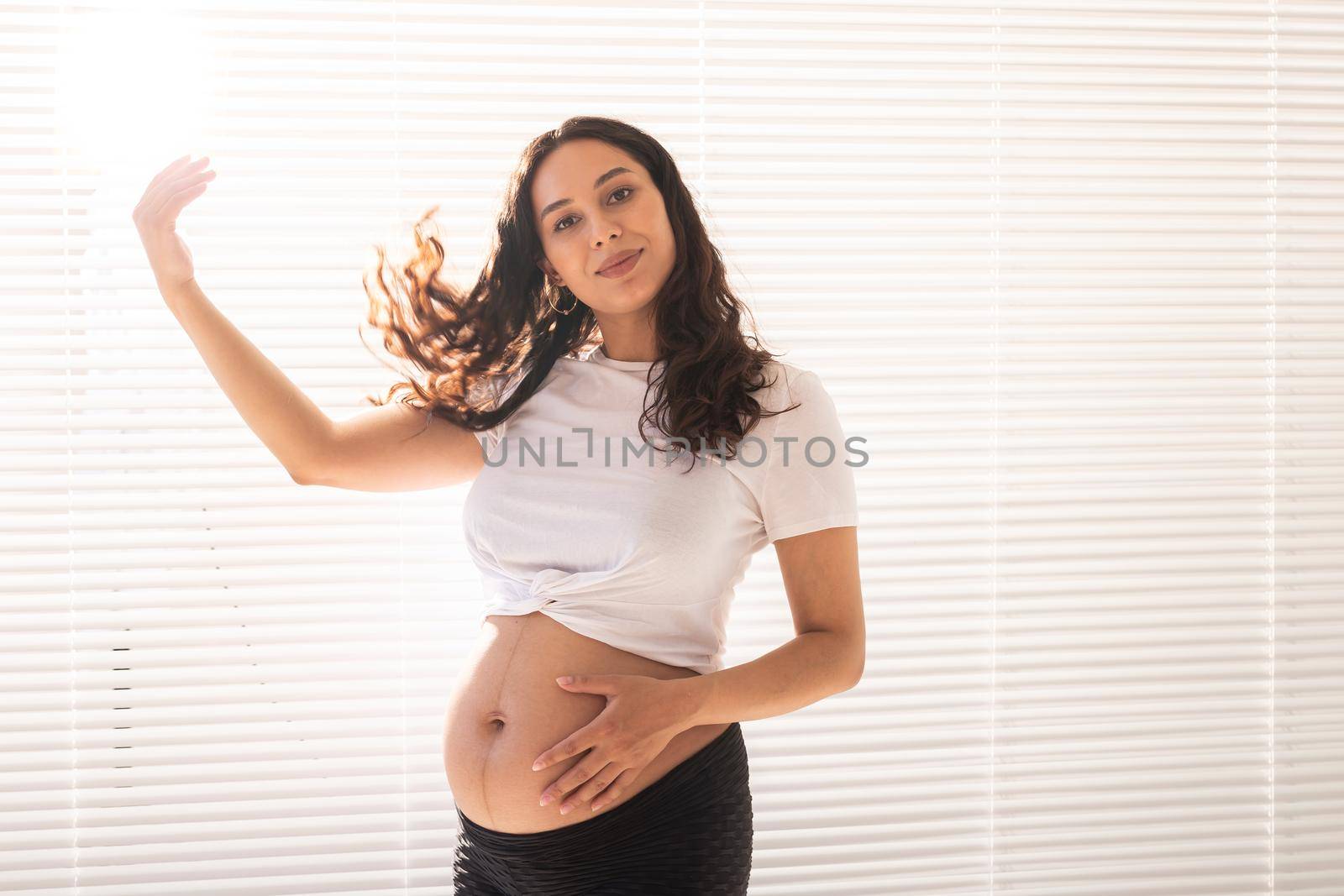 Smiling young beautiful pregnant woman touching her belly and hair and rejoicing. Health and thinking about the future while waiting for baby. Copyspace