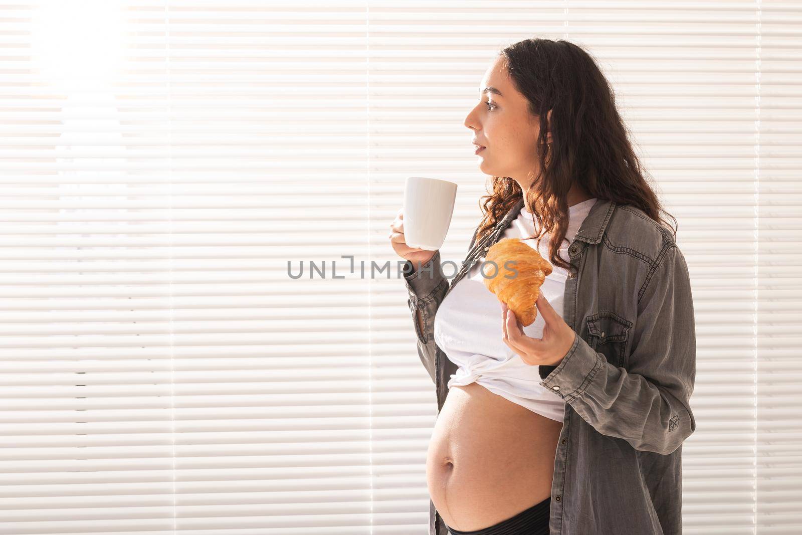 Healthy beautiful pregnant woman drinking tea and eating croissant during lunch. High-calorie nutrition while waiting for birth of baby