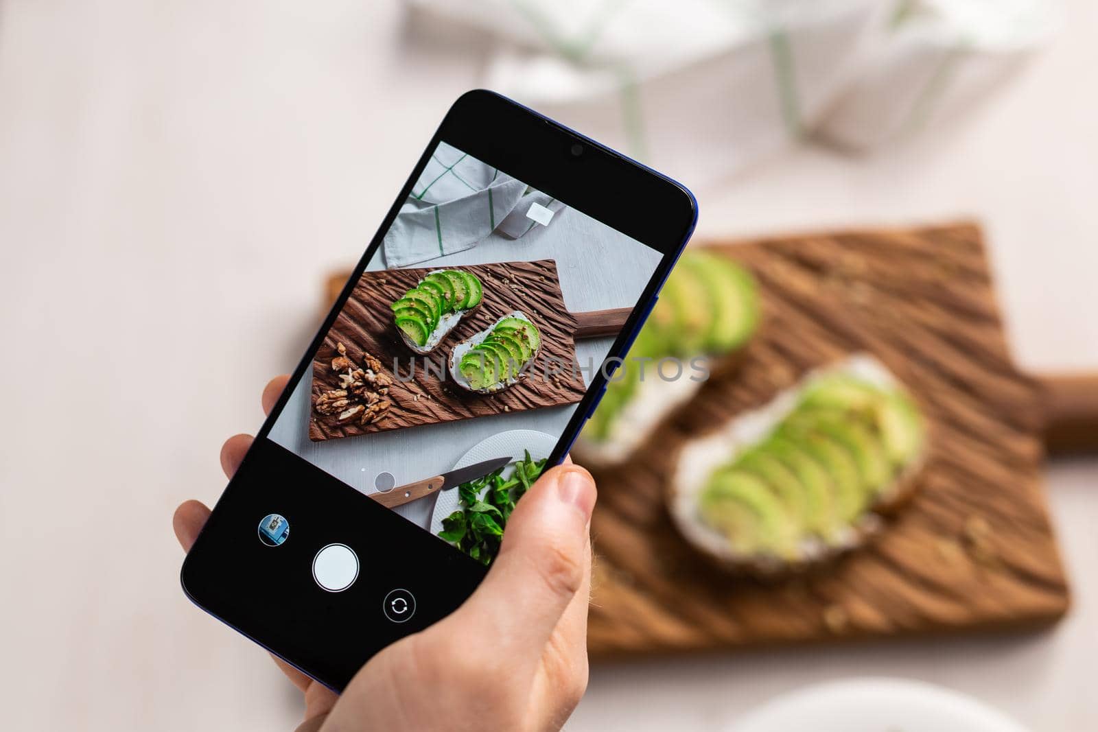 Hands take pictures on smartphone of two beautiful healthy sour cream and avocado sandwiches lying on board on the table. Social media and food