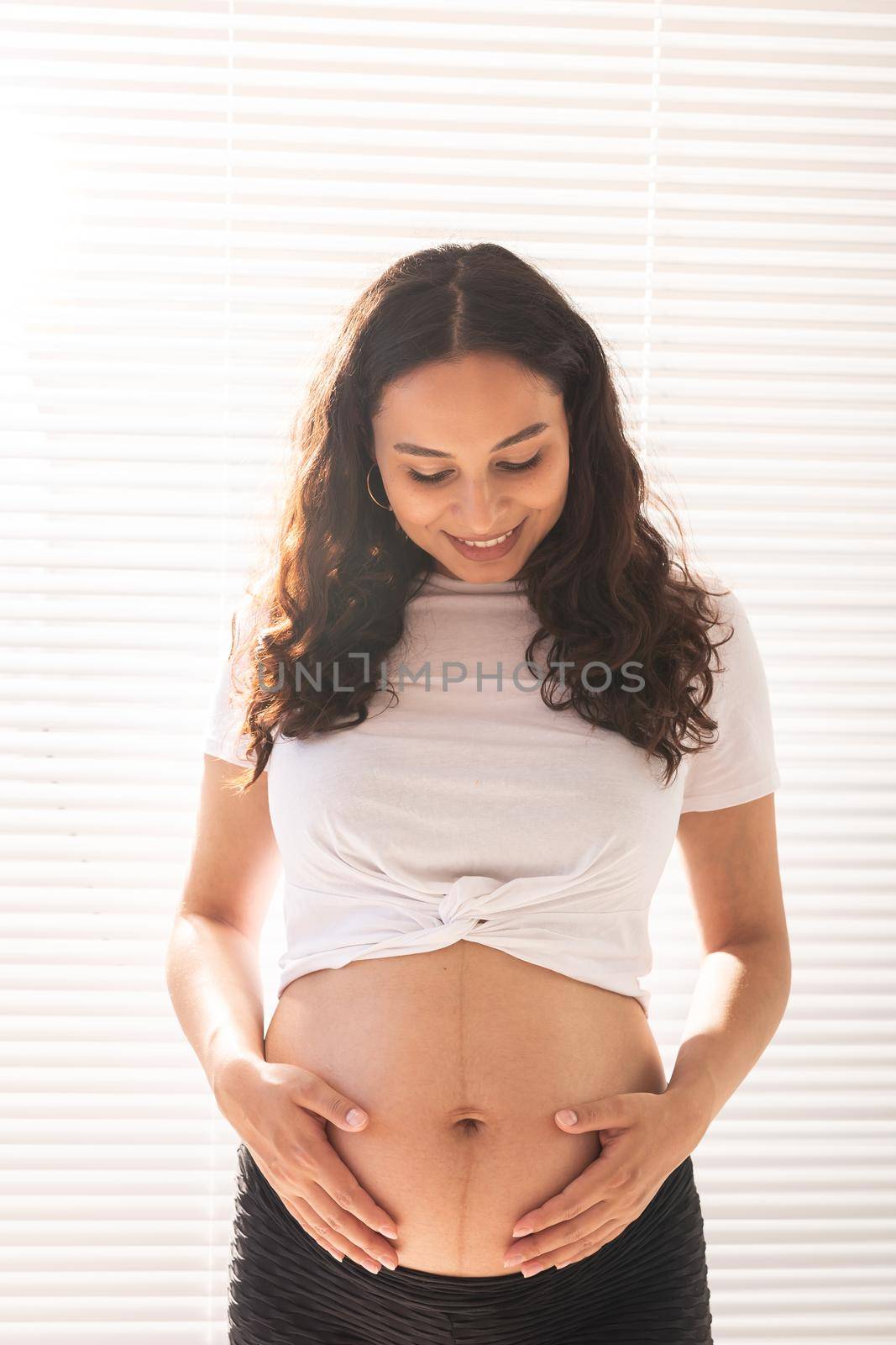 Smiling young beautiful pregnant woman touching her belly and rejoicing. Concept of positive and pleasant feelings while waiting for the baby.