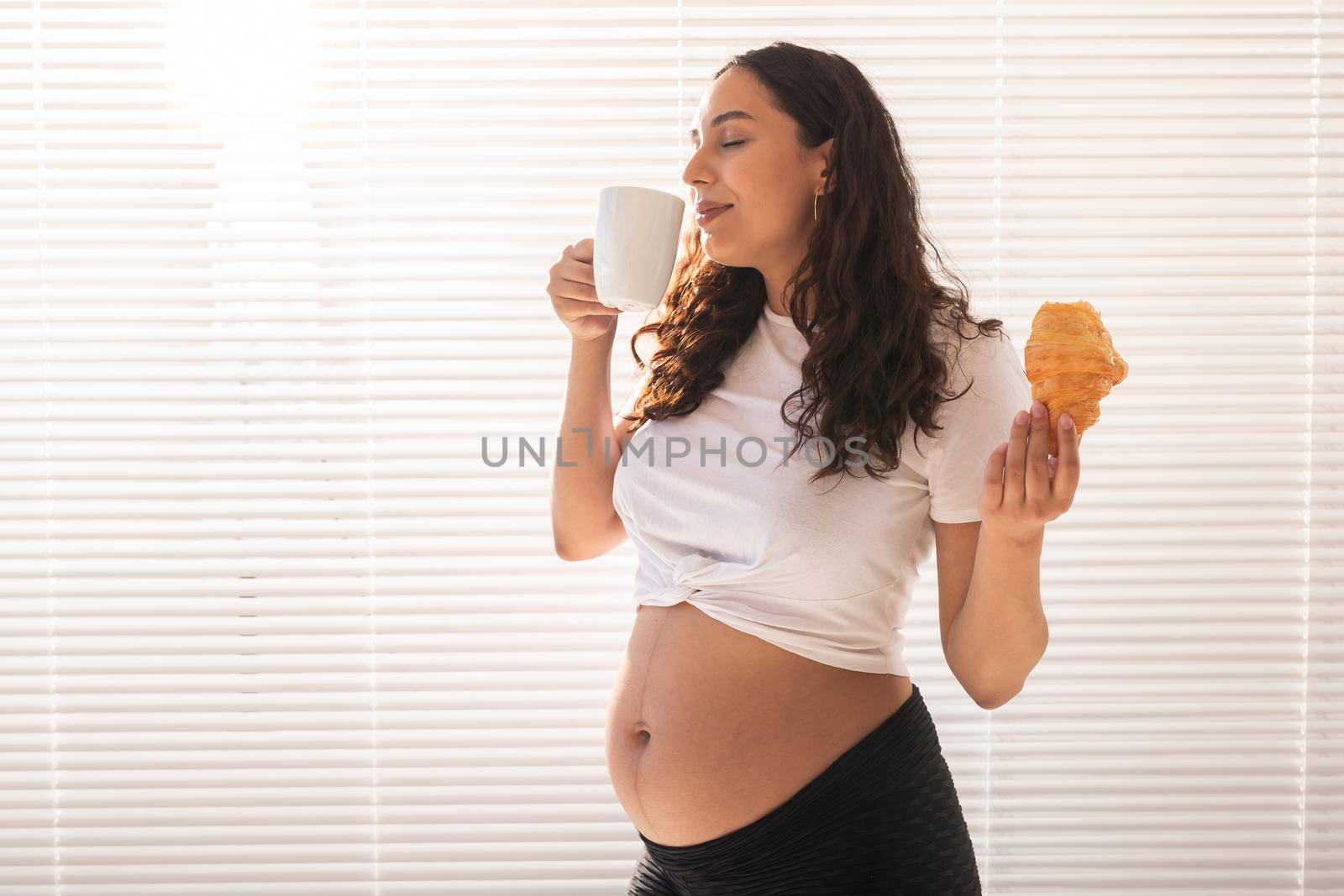 Happy pregnant woman with croissant buns at home. Pregnancy, eating and people