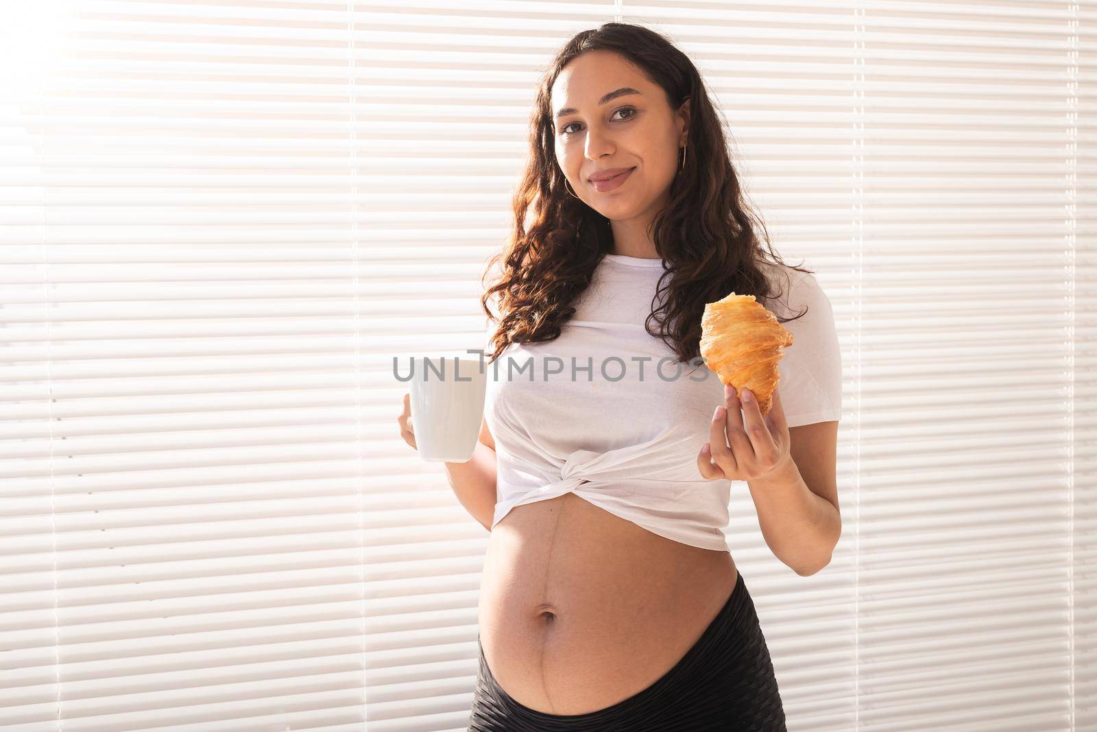 Happy pregnant woman with croissant buns at home. Pregnancy, eating and people