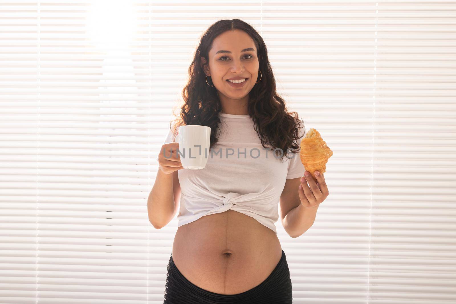 Pregnant woman eating croissant and drinks coffee. Pregnancy and maternity leave.