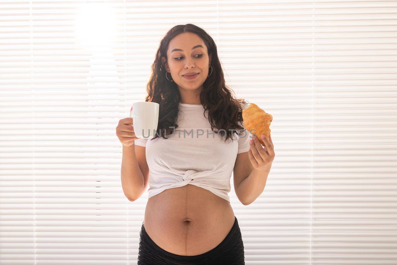 Happy pregnant woman with croissant buns at home. Pregnancy, eating and people