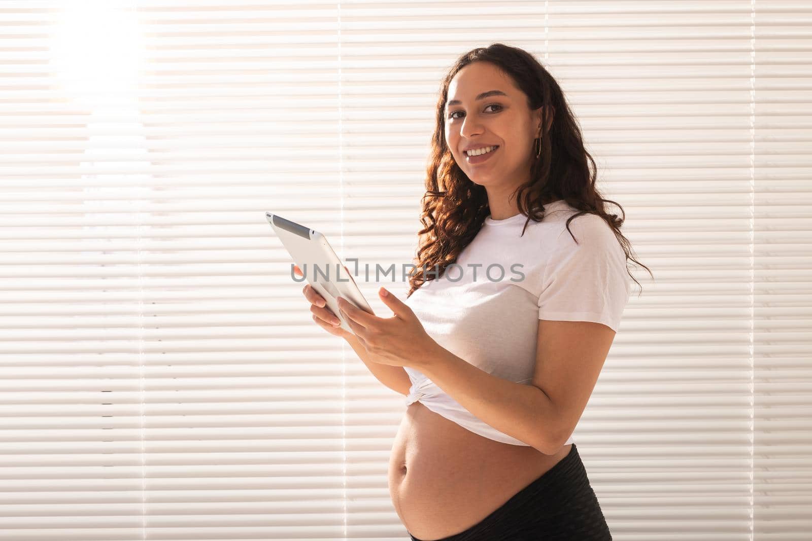 Happy pregnant young beautiful woman talking to her husband using video connection and tablet. Communication and positive attitude during pregnancy