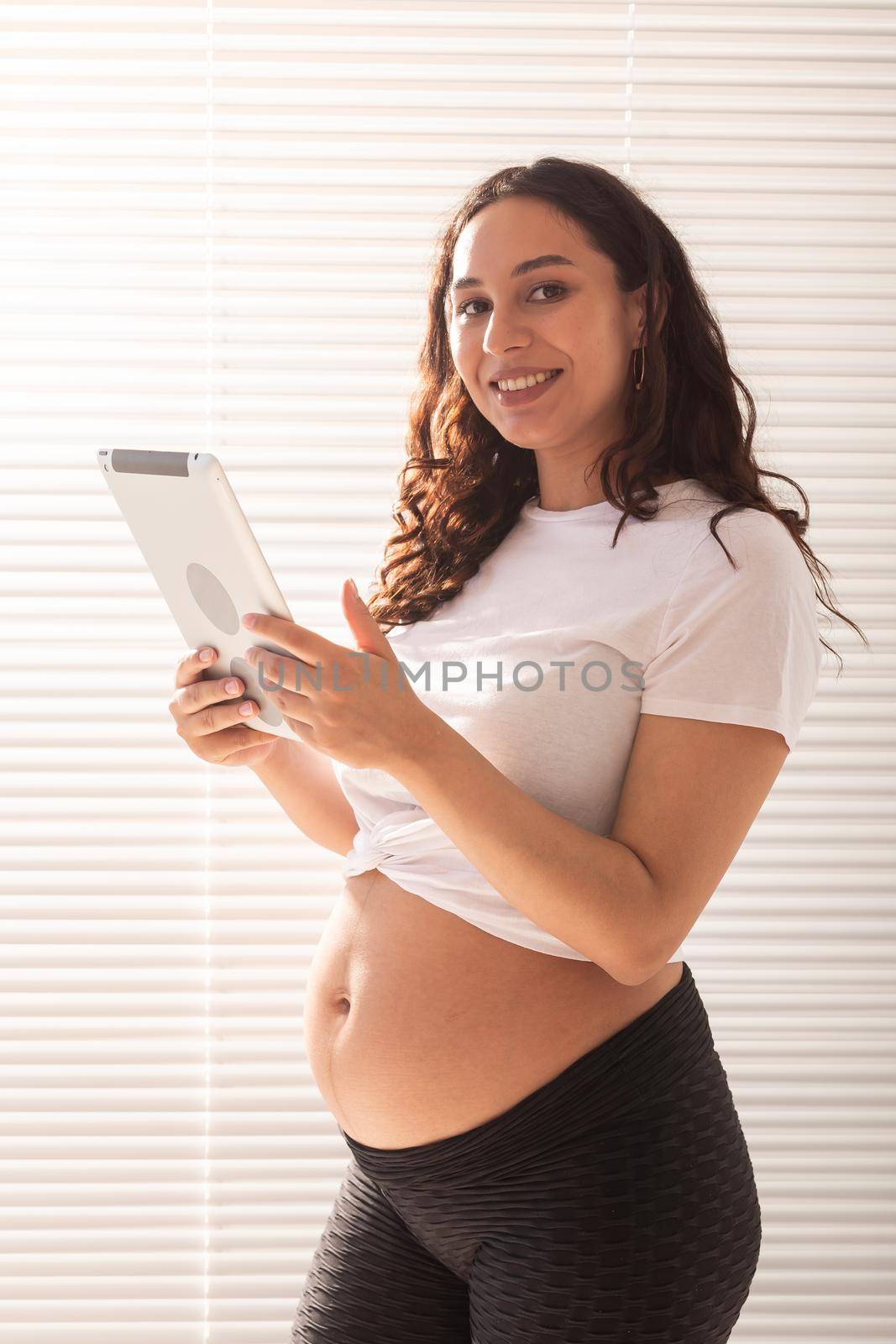 Happy pregnant young beautiful woman talking to her husband using video connection and tablet. Communication and positive attitude during pregnancy