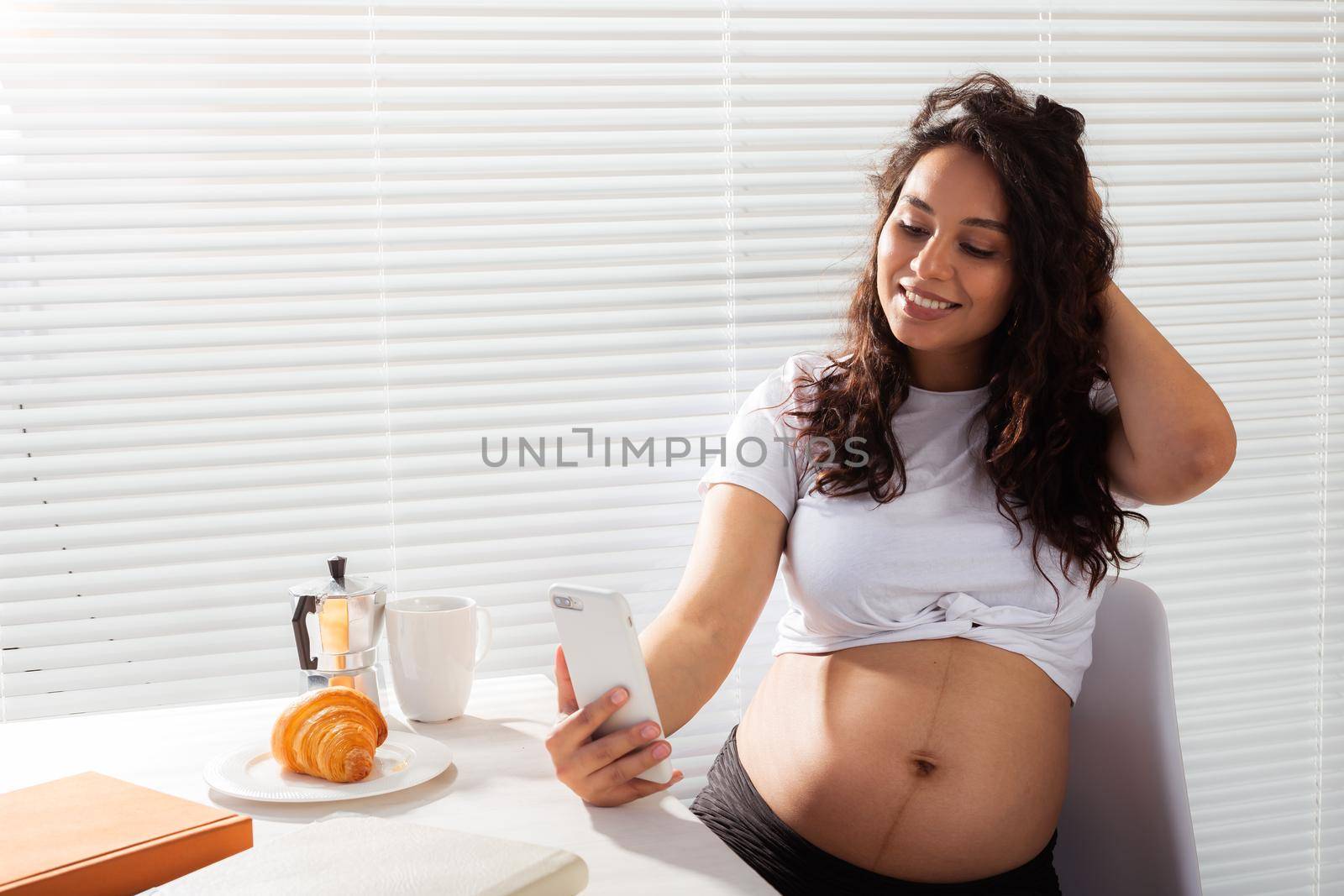 Pregnant woman taking a self portrait with her smartphone while breakfast.