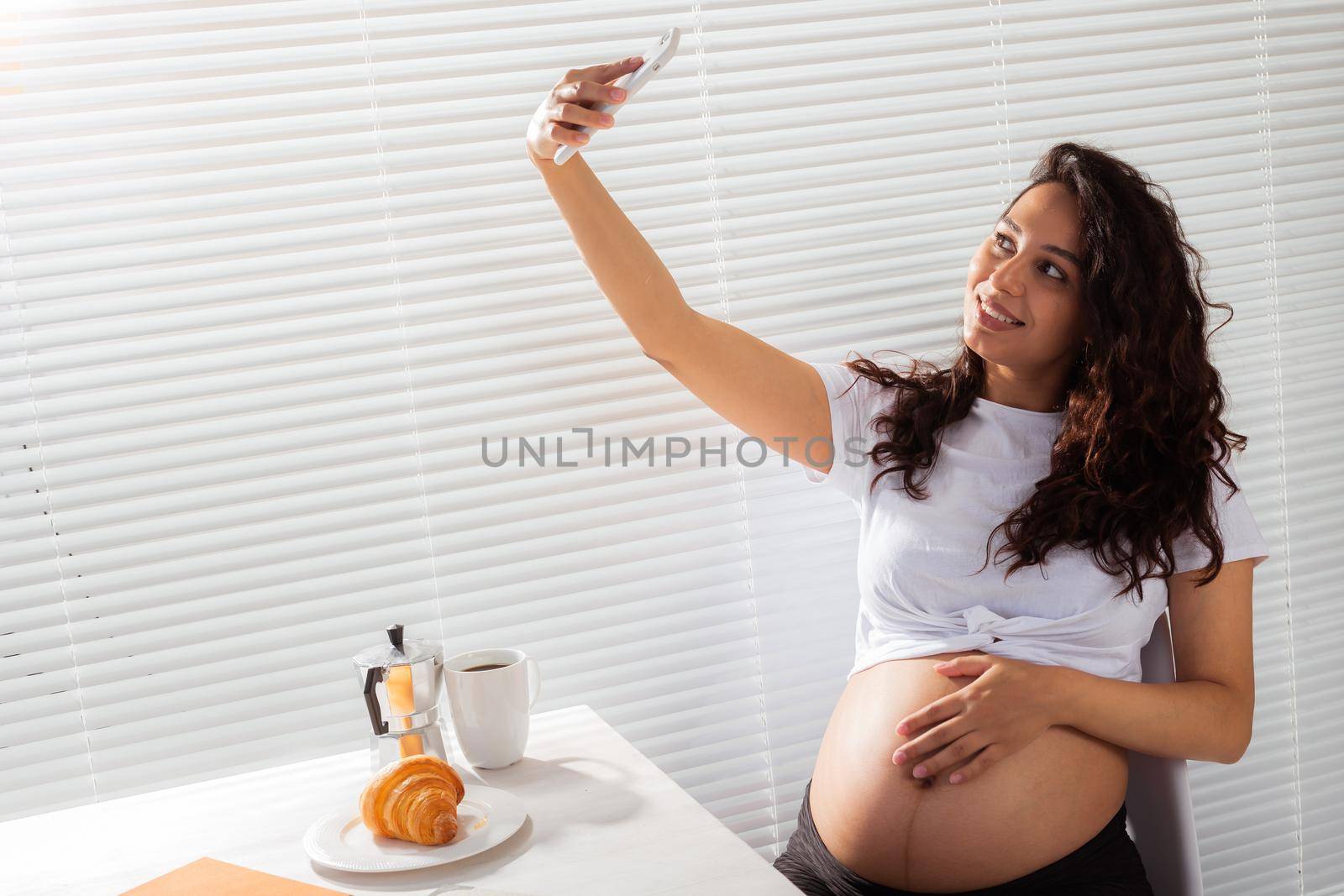 Pregnant woman taking a self portrait with her smartphone while breakfast.