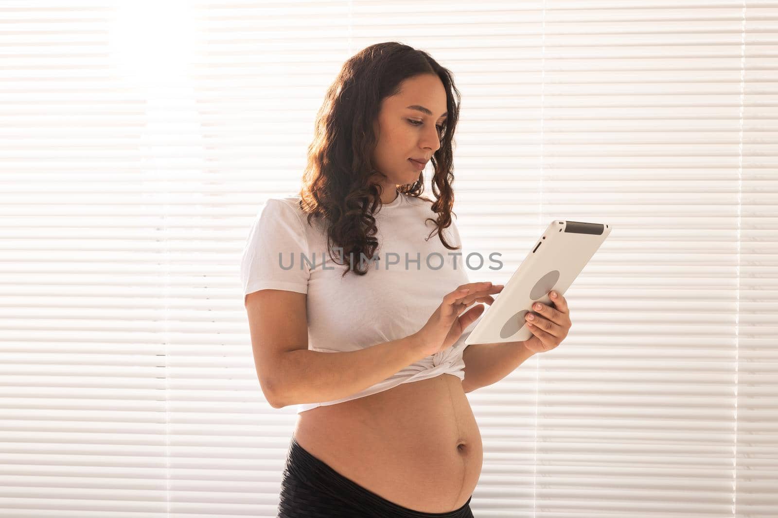 Happy pregnant young beautiful woman talking to her husband using video connection and tablet. Communication and positive attitude during pregnancy