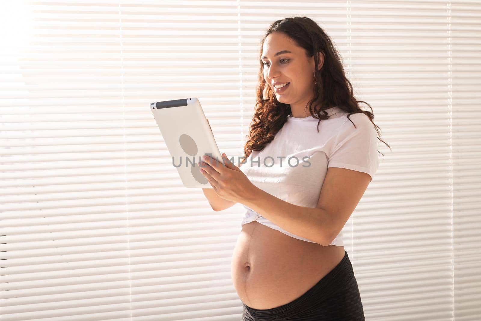 Happy pregnant young beautiful woman talking to her husband using video connection and tablet. Communication and positive attitude during pregnancy