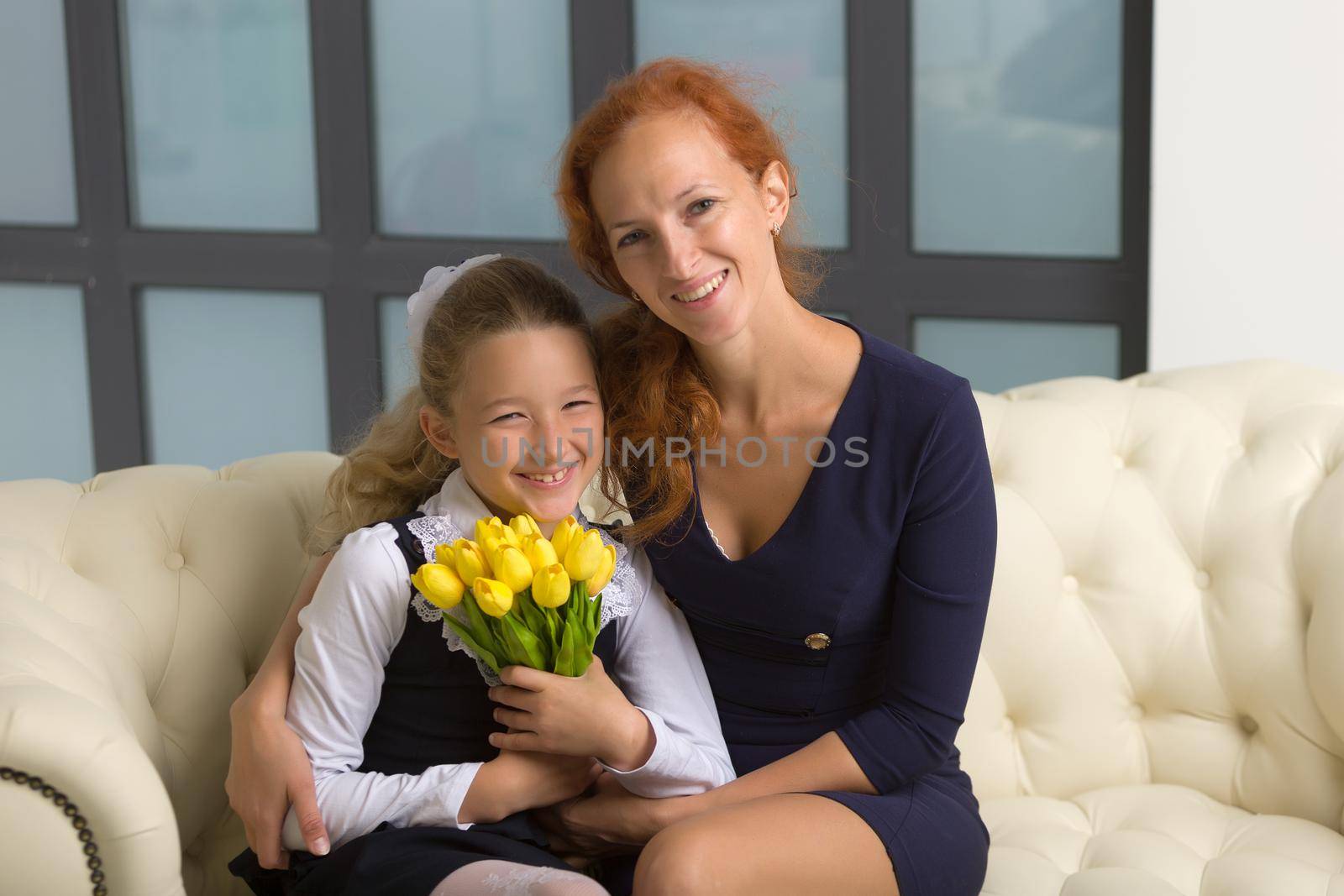 A beautiful young mother and little daughter near a bouquet of tulips, which her daughter gave to her mother for the holiday. The concept of women's holiday, family values.