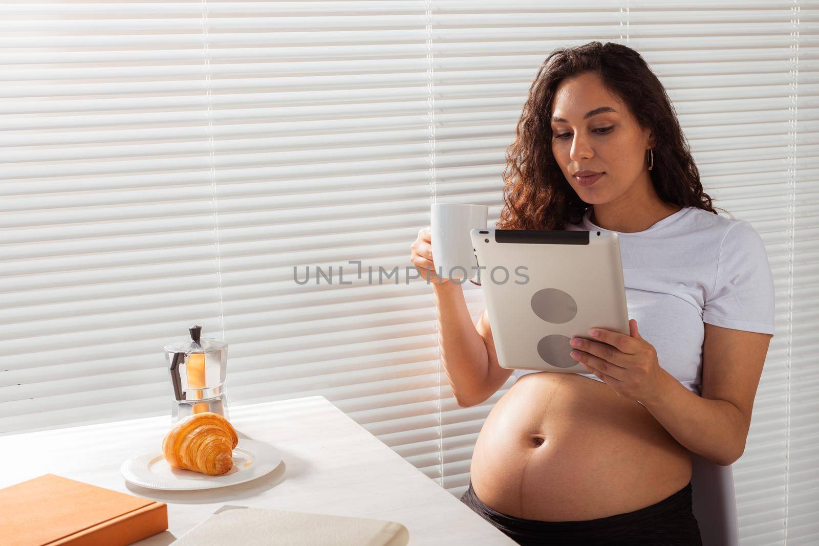 Pregnant woman using digital tablet. Breakfast time. Technology and pregnancy