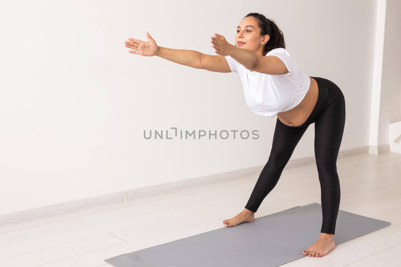 Young flexible pregnant woman doing gymnastics on rug on the floor on white background. Preparing the body for easy childbirth