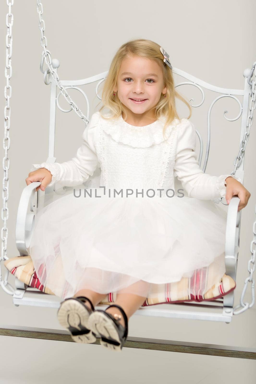 Beautiful little girl swinging in the studio on a swing. Concept of a happy childhood, family well-being.