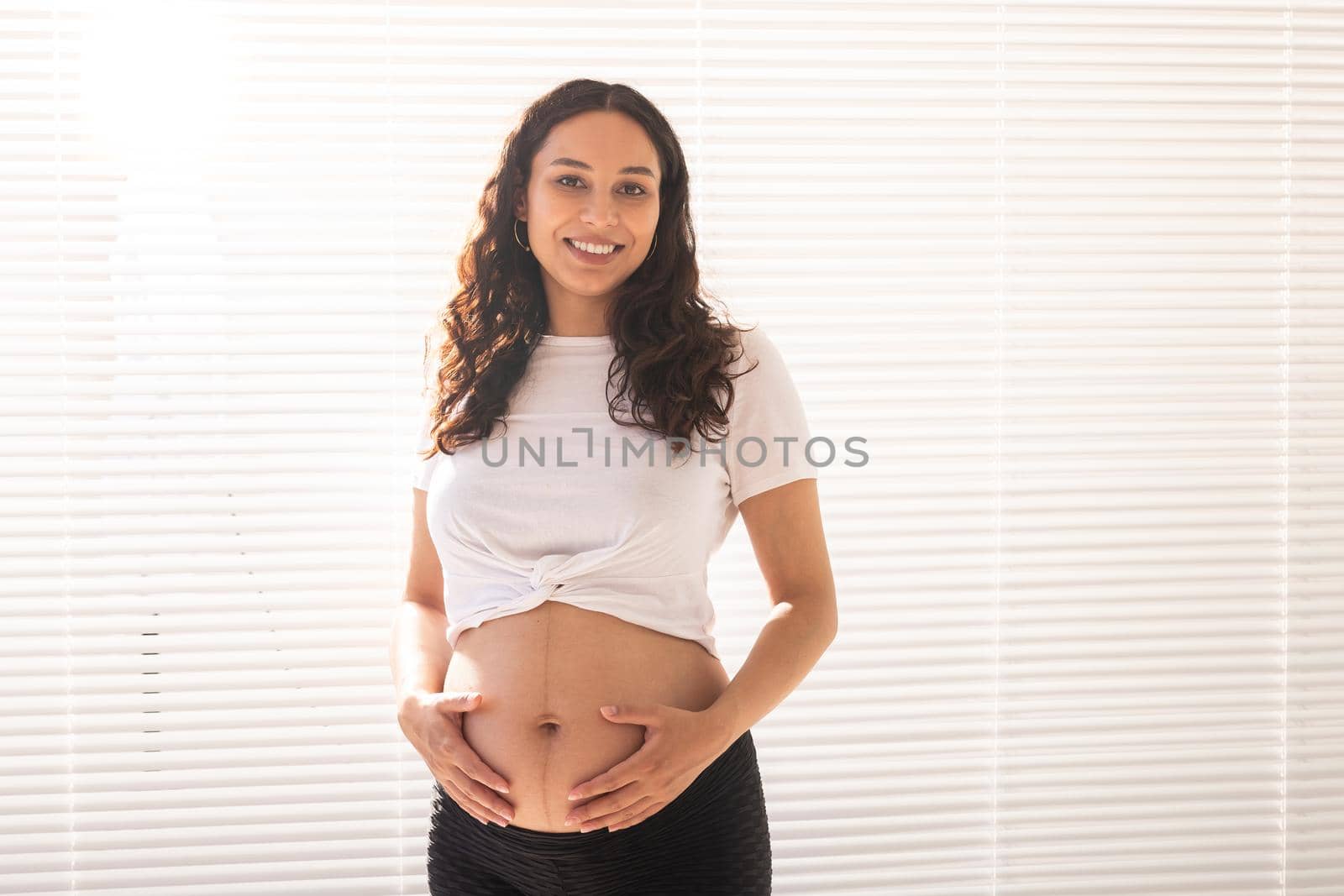 Smiling young beautiful pregnant woman touching her belly and rejoicing. Concept of positive and pleasant feelings while waiting for the baby.