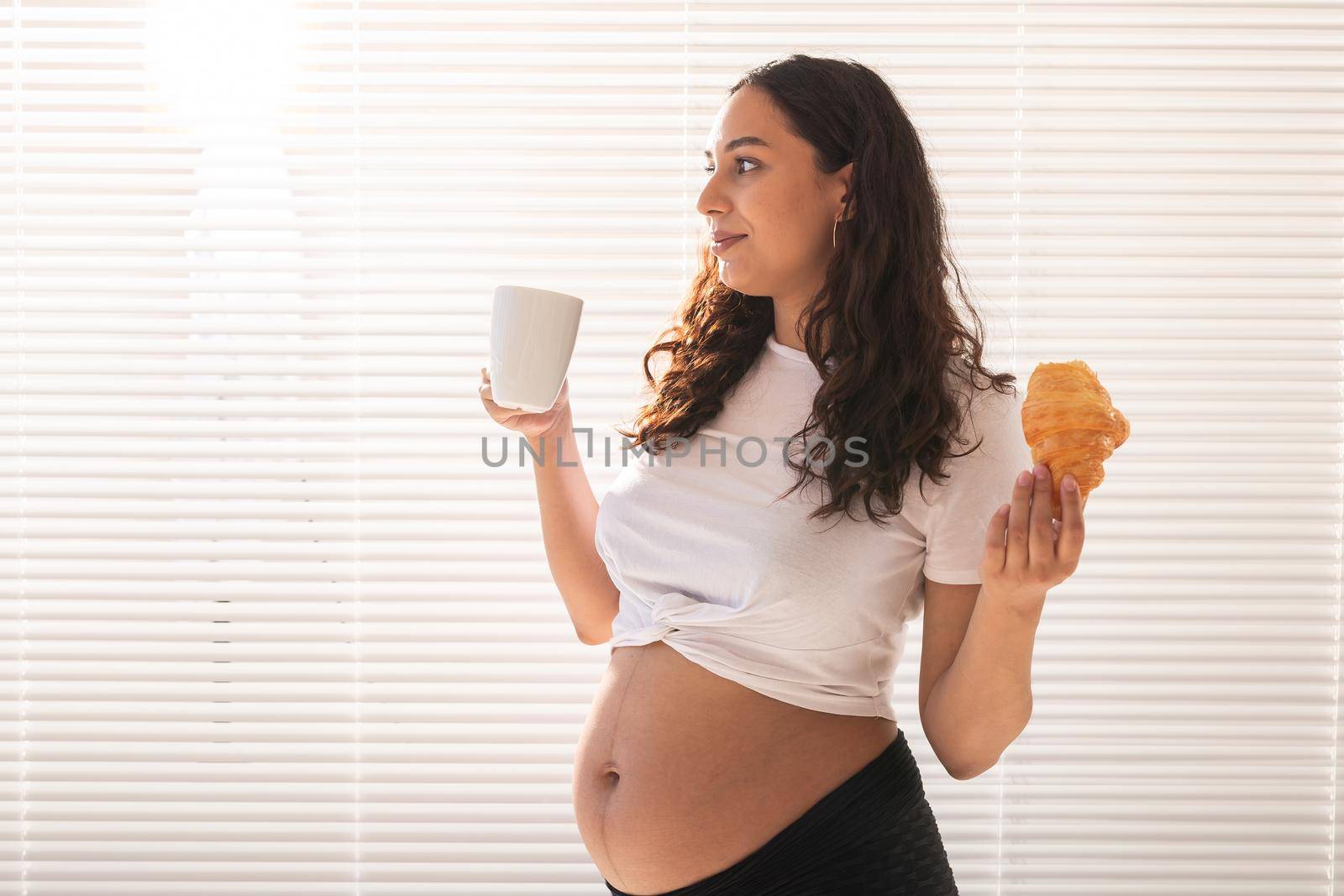Happy pregnant woman with croissant buns at home. Pregnancy, eating and people