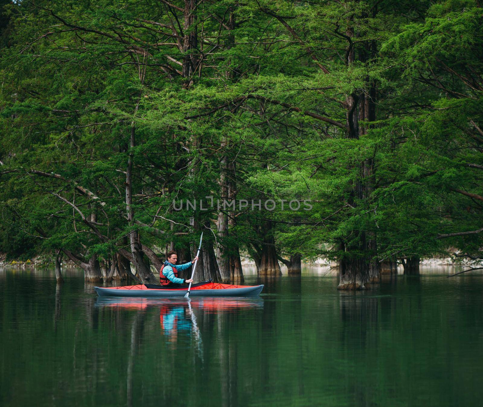 Explorer young man paddling in kayak on lake near the cypresses in summer