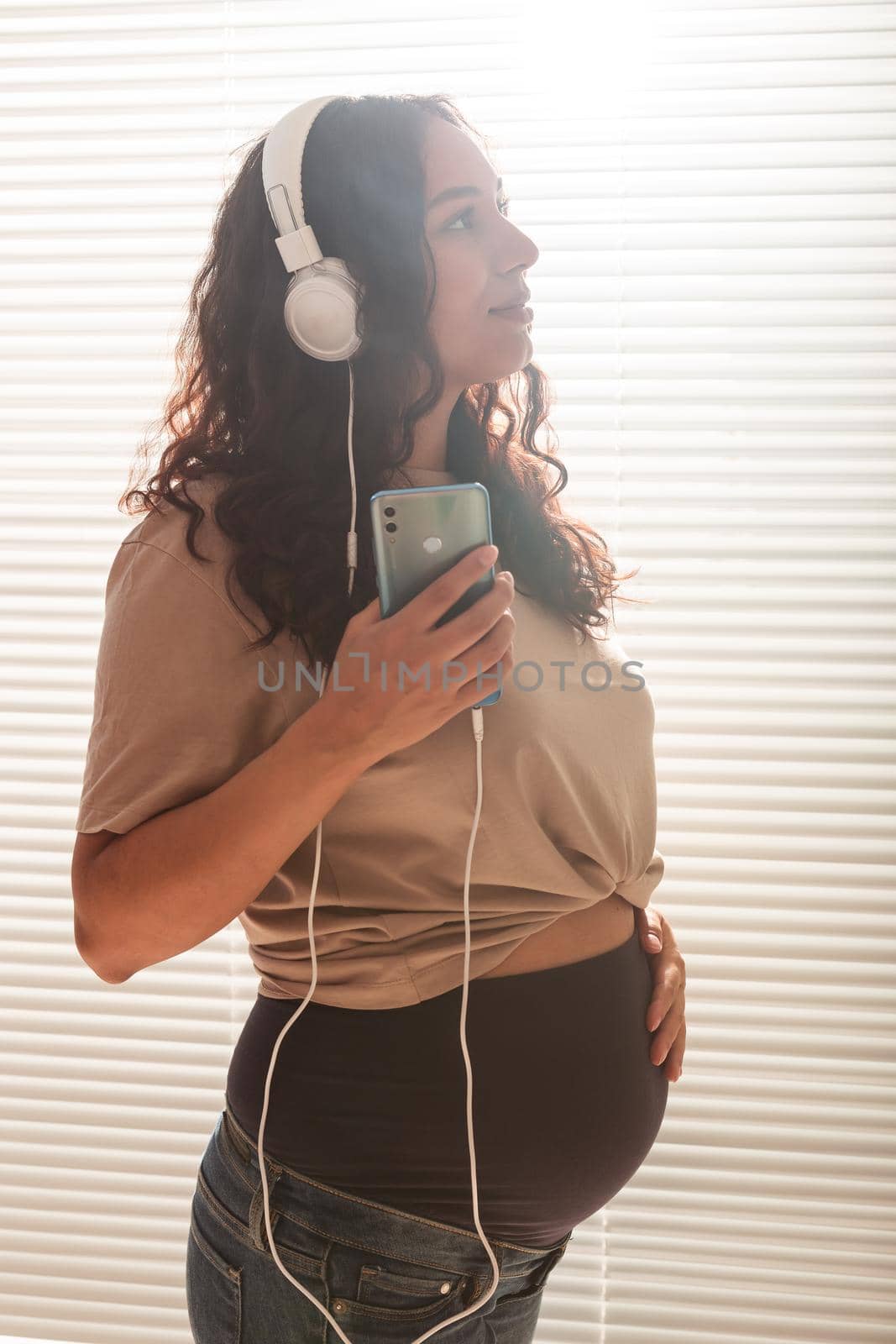 Happy pregnant woman with curly hair listening music in headphones.