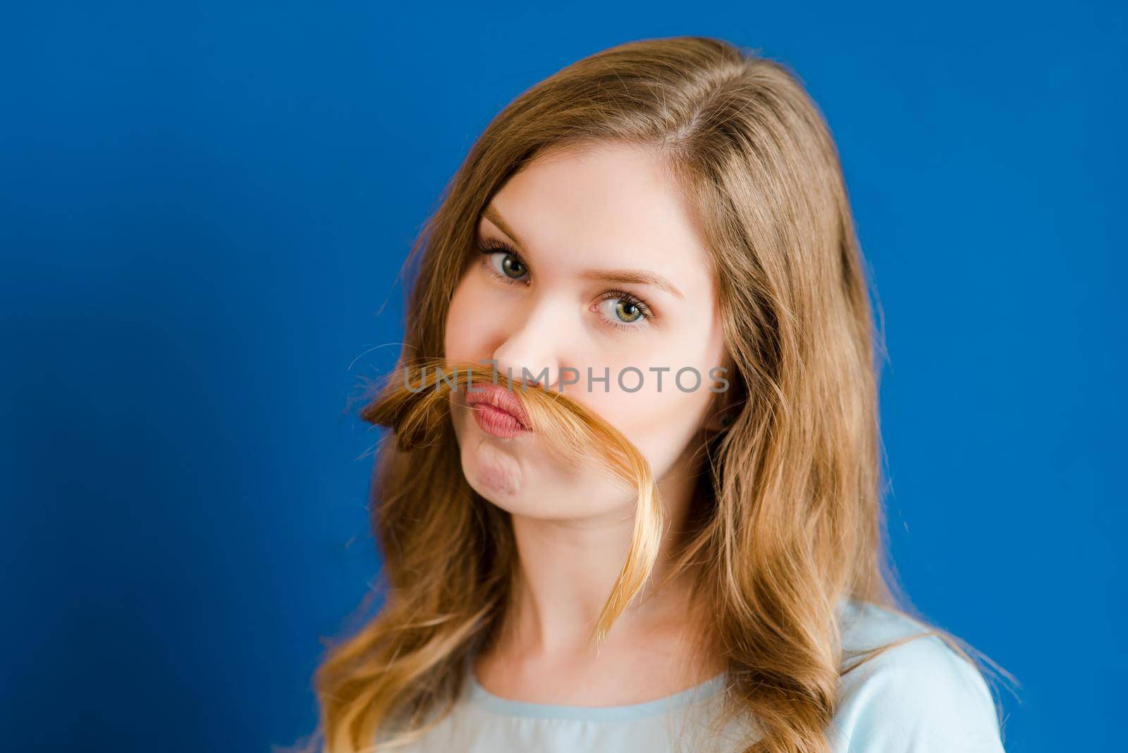 A girl on a blue background has a mustache made of hair