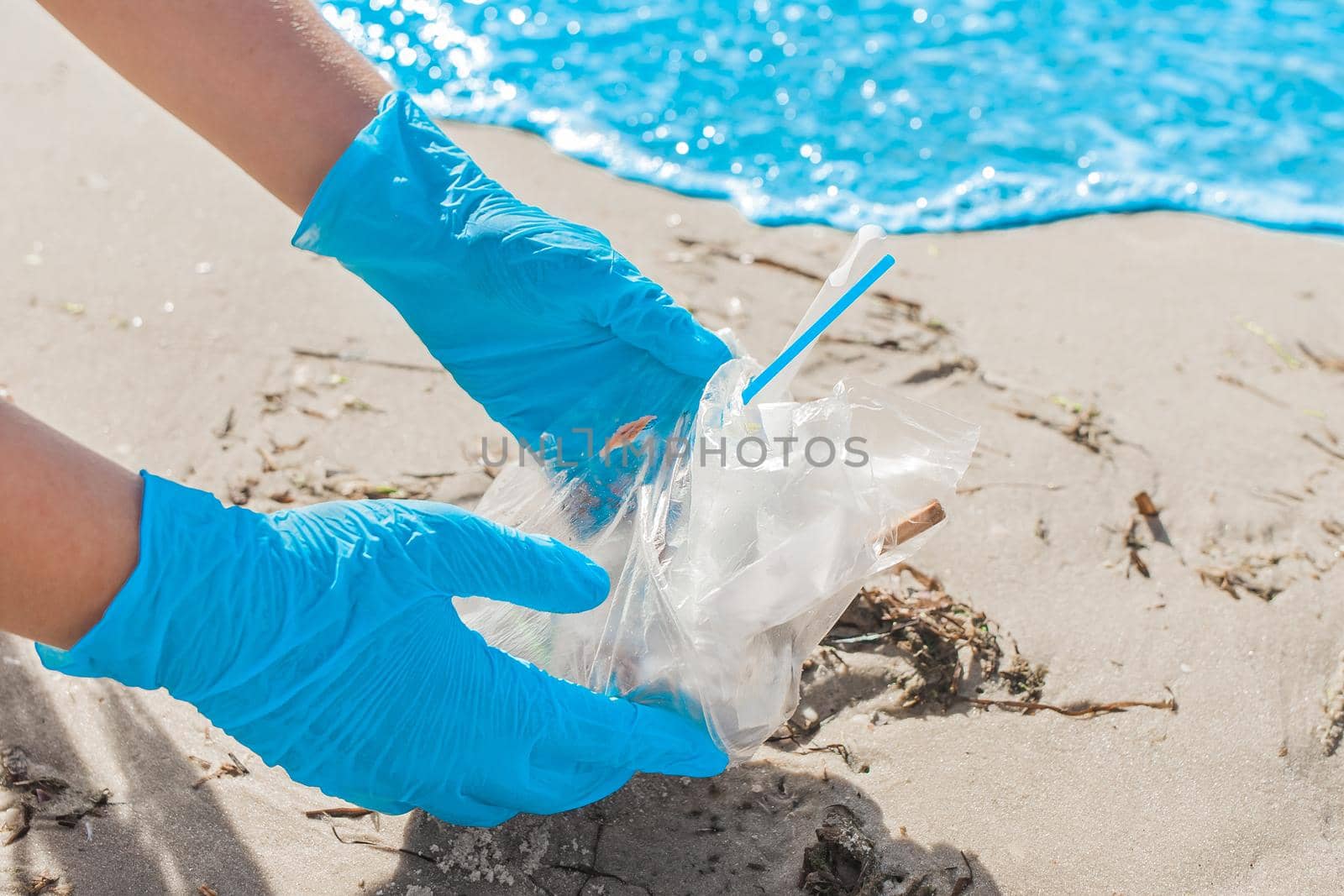 The girl's hands in blue protective home gloves remove garbage on the sea shore near the water close-up. Pollution of the environment and the environment.