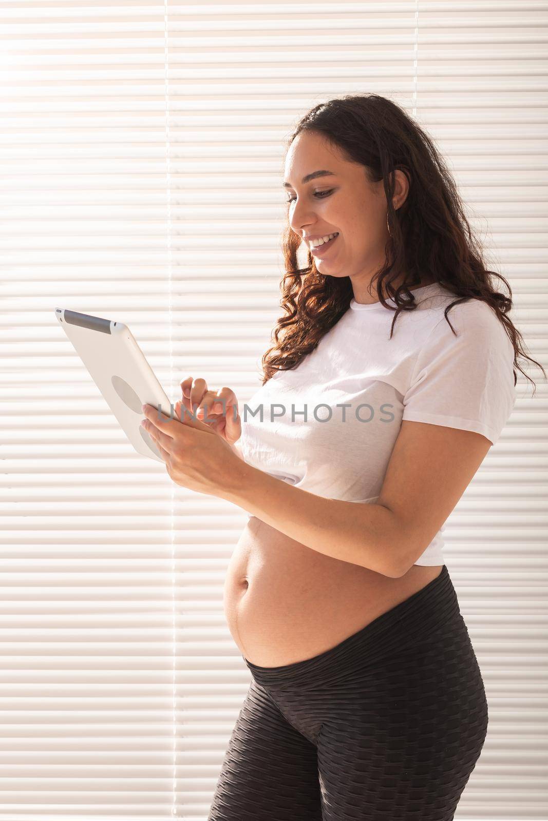 Happy pregnant young beautiful woman talking to her husband using video connection and tablet. Communication and positive attitude during pregnancy
