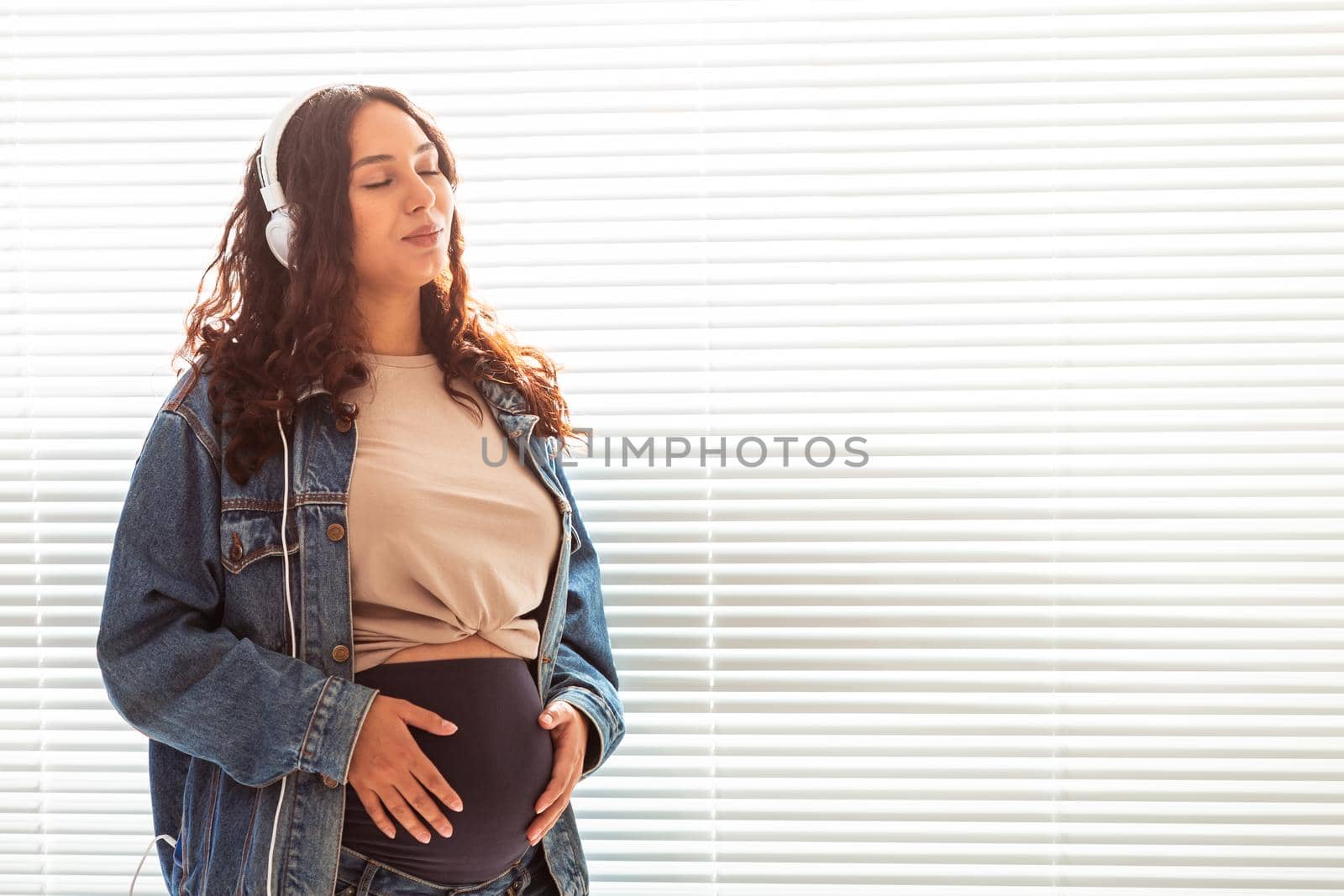 Young peaceful pregnant woman listens to pleasant classical music using smartphone and headphones. Concept of positive attitude before childbirth