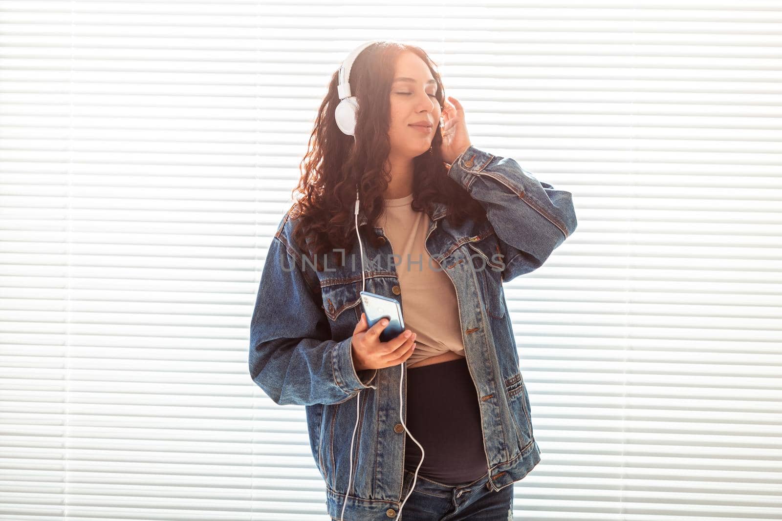 Young peaceful pregnant woman listens to pleasant classical music using smartphone and headphones. Concept of positive attitude before childbirth