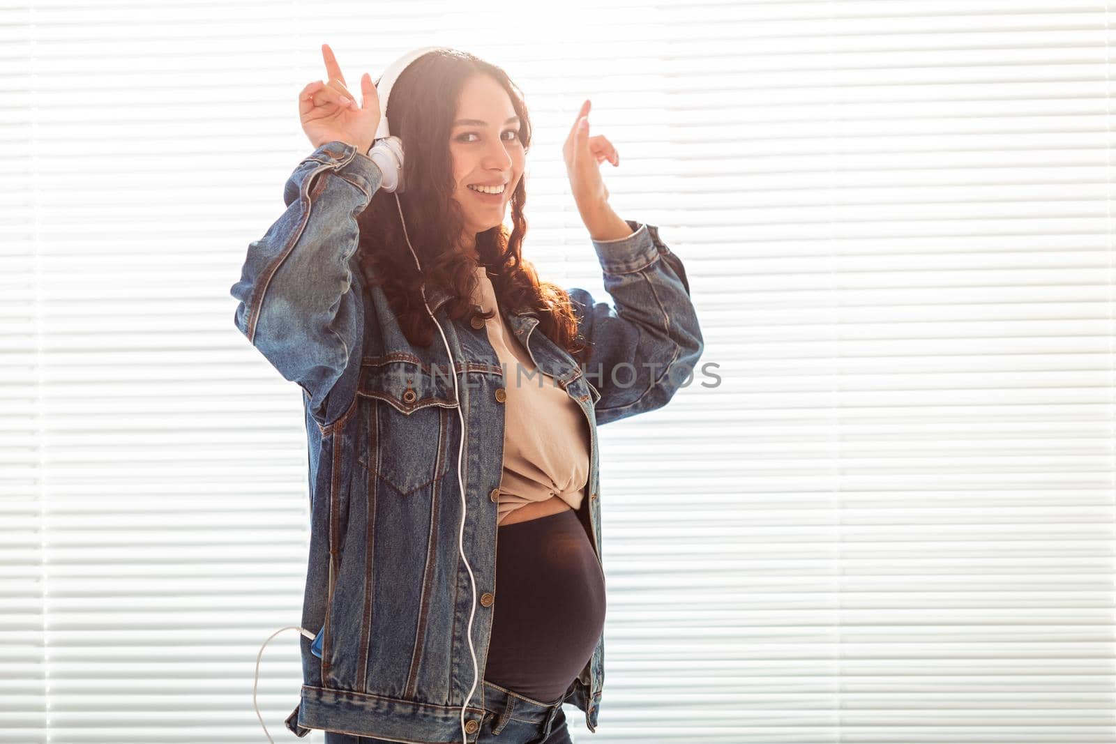 Young peaceful pregnant woman listens to pleasant classical music using smartphone and headphones. Concept of positive attitude before childbirth