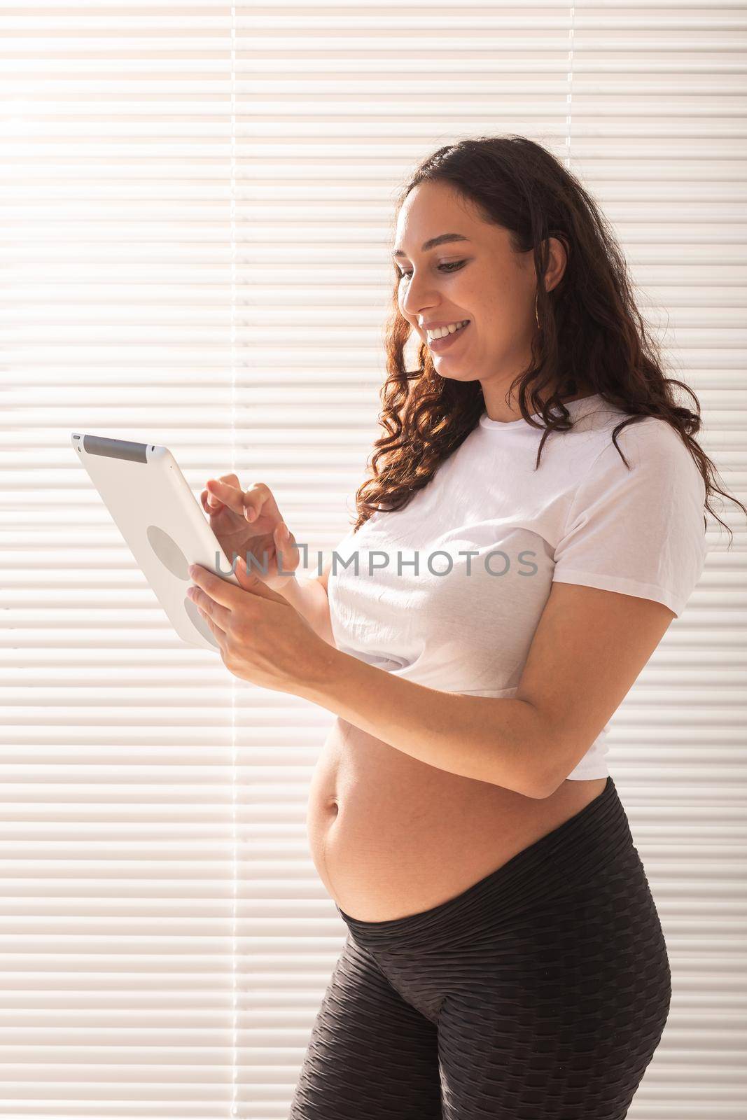 Happy pregnant young beautiful woman talking to her husband using video connection and tablet. Communication and positive attitude during pregnancy