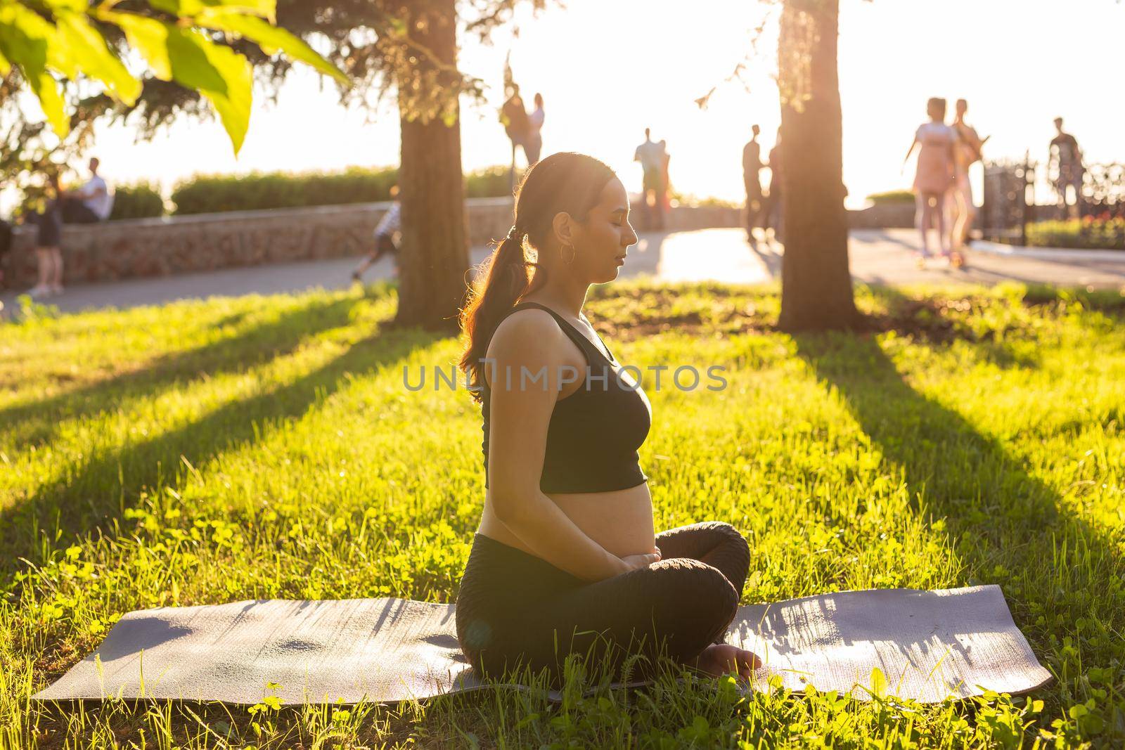 Cute young caucasian pregnant woman is meditating while sitting on a rug on the lawn on a sunny summer evening. Concept of pacification