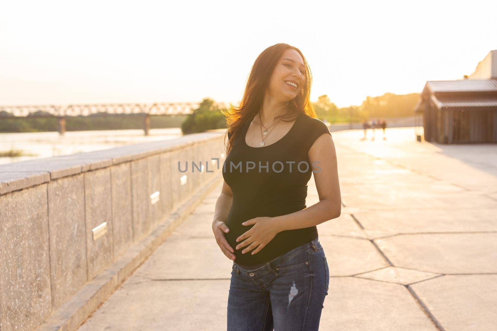 Portrait of a happy pregnant woman looking at side walking in a park at sunset. Pregnancy and motherhood