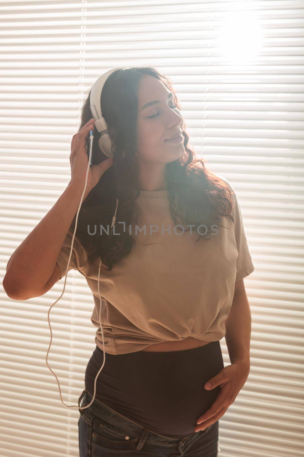 Portrait of pregnant woman sitting on sofa at home and listening music in headphones.