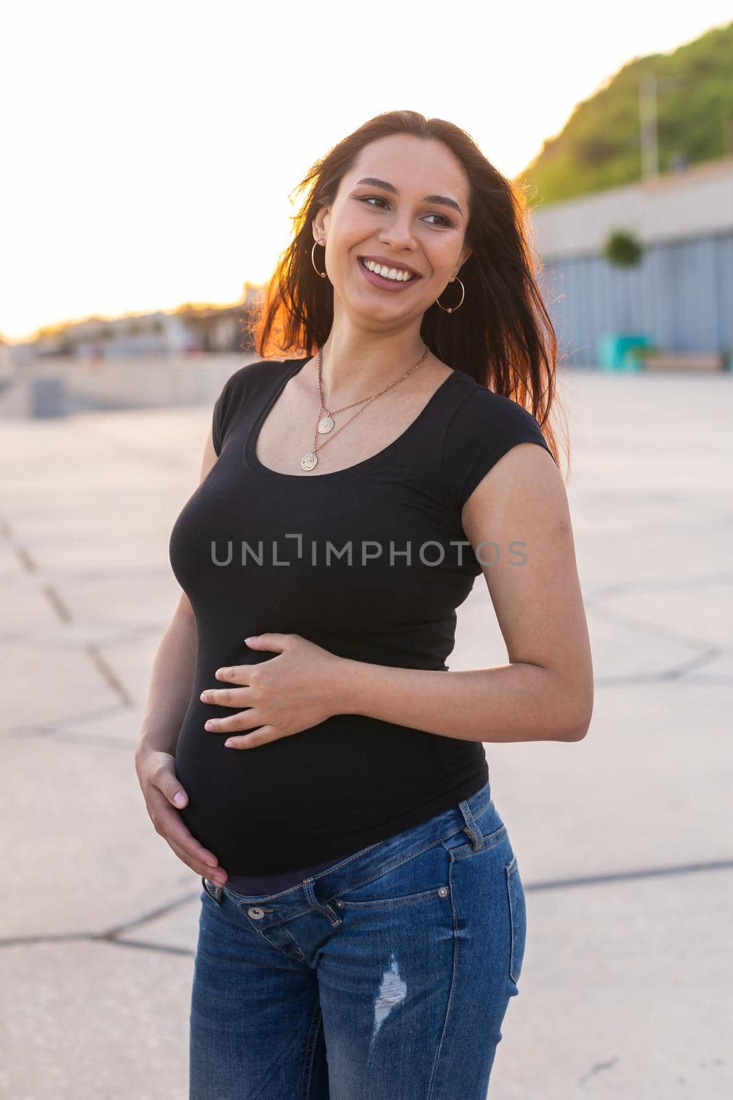 Portrait of a happy pregnant woman looking at side walking in a park at sunset. Pregnancy and motherhood