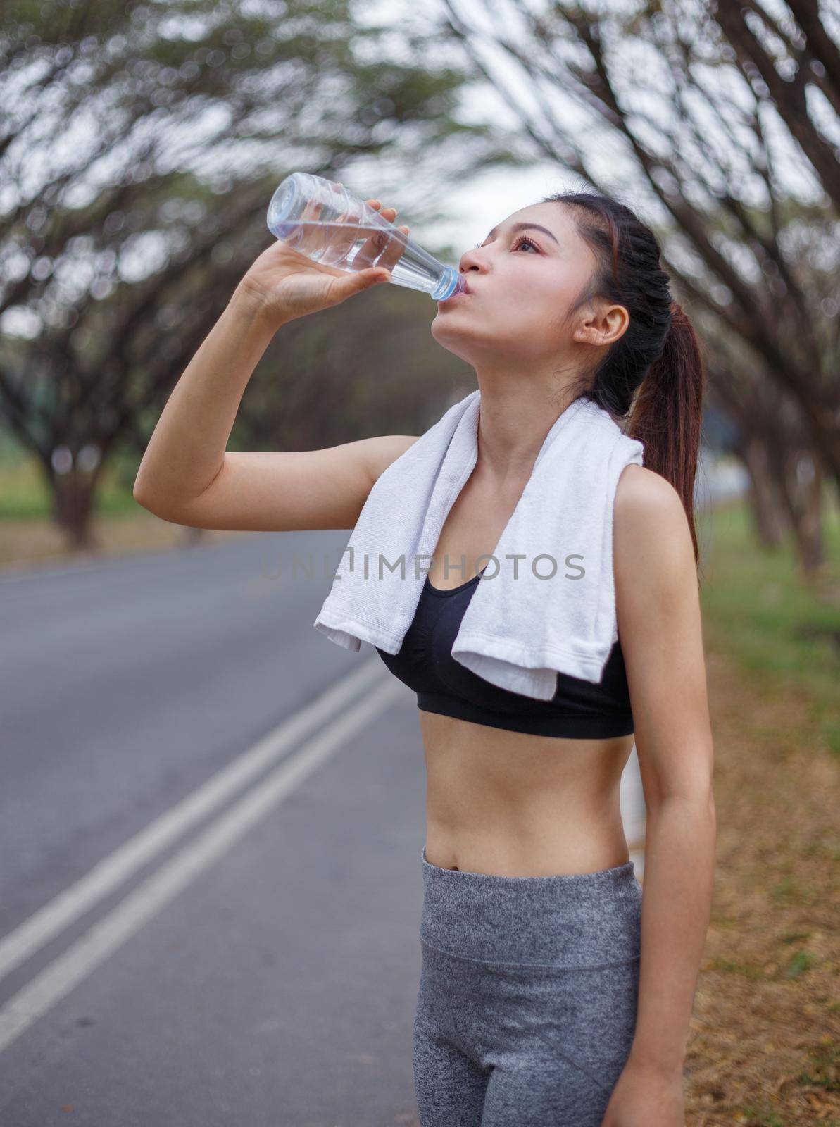 young sporty woman drinking water in park by geargodz