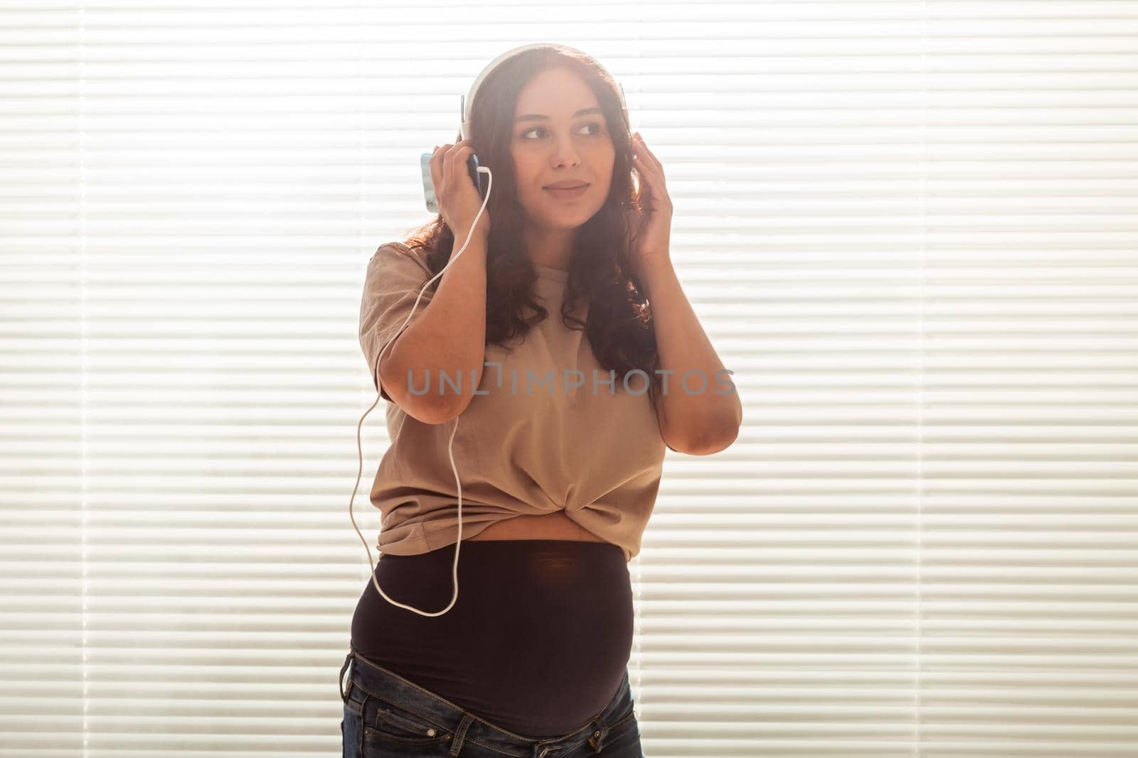 Portrait of pregnant woman sitting on sofa at home and listening music in headphones.