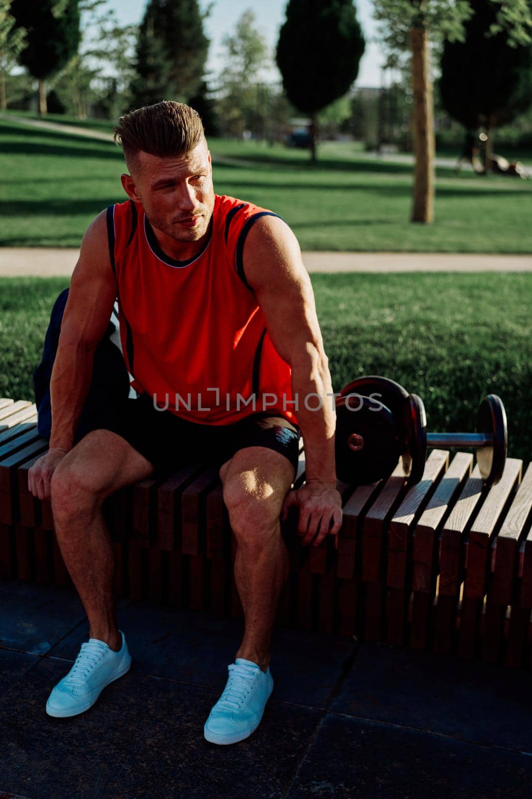 Cheerful male athlete in the park sits on a bench. High quality photo