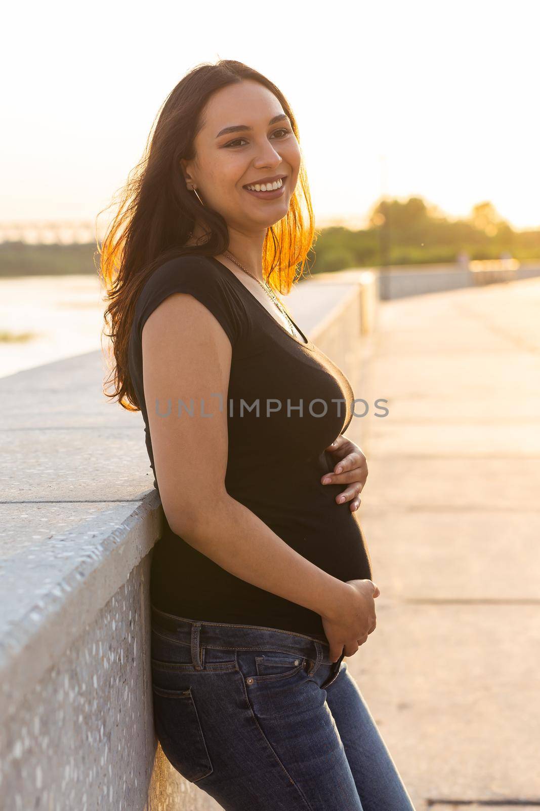 Portrait of a happy pregnant woman looking at side walking in a park at sunset. Pregnancy and motherhood