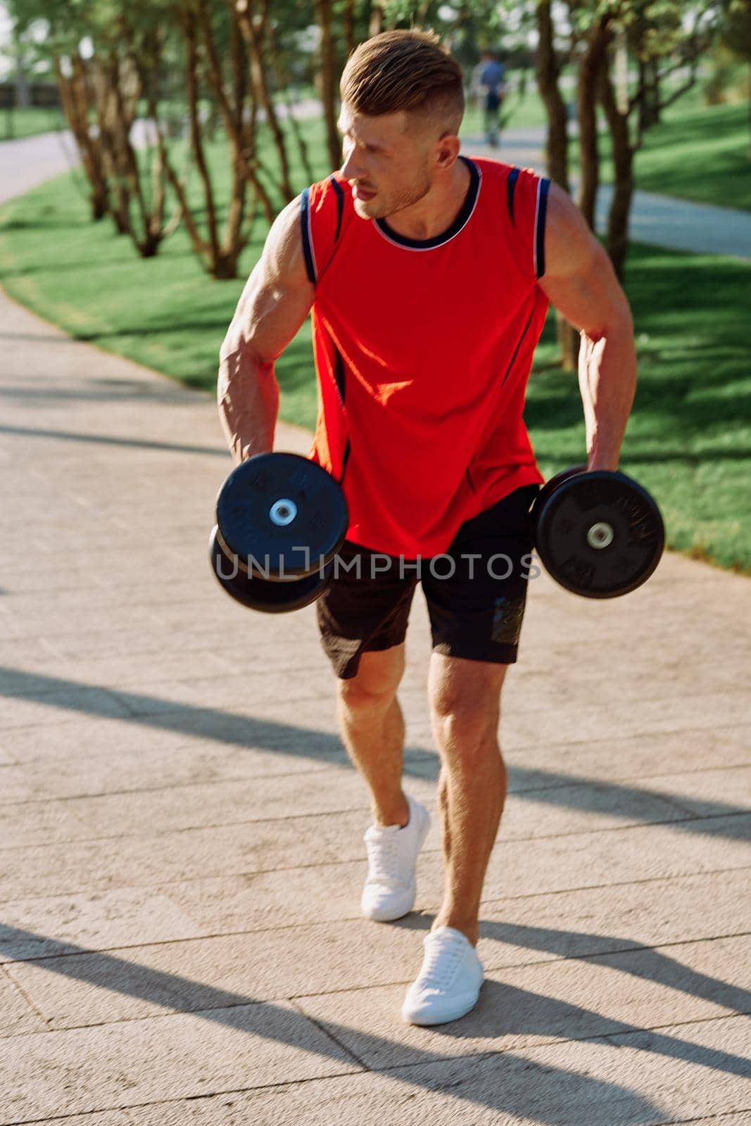 athletic man with dumbbells in his hands outdoors in the park by Vichizh