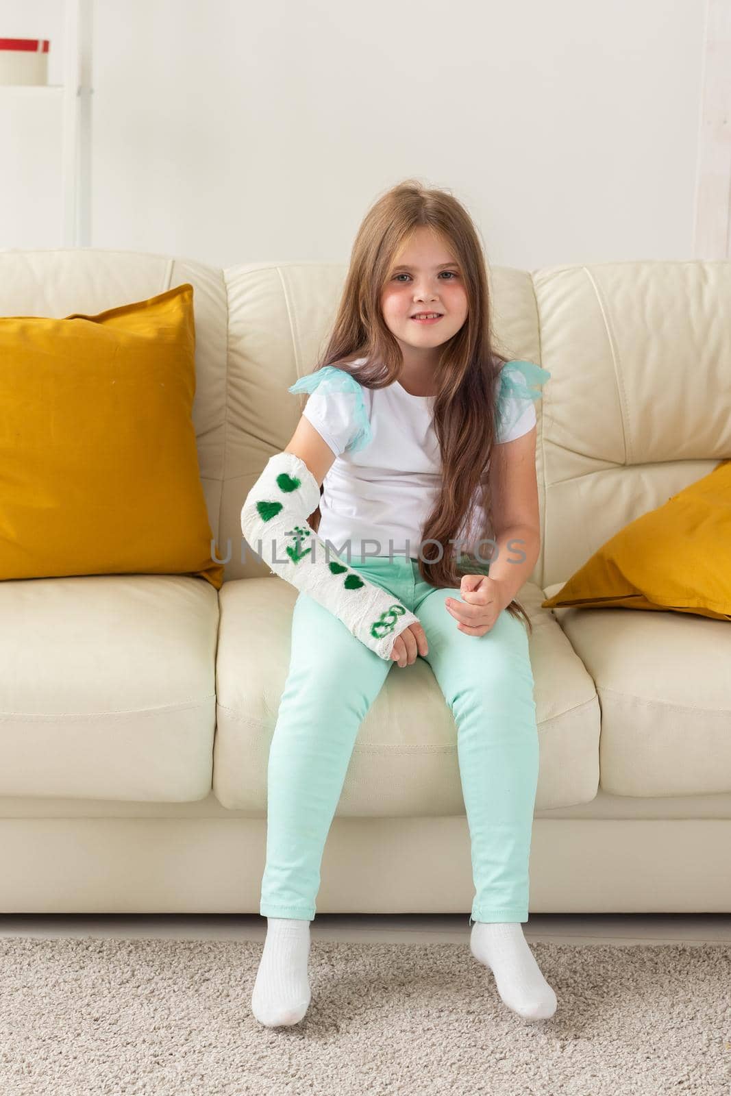 Child with a cast on a broken wrist or arm smiling and having fun on a couch. Positive attitude, recovery and kid.