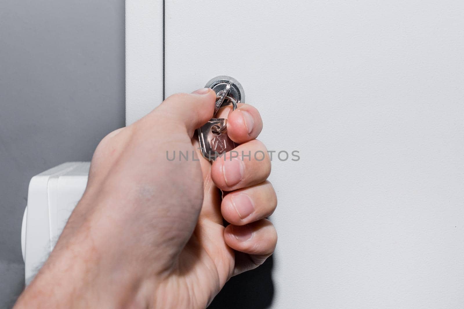 The hand of a human electrician opens or closes the electrical box with a metal key. Safe technologies and control system of electrical equipment.