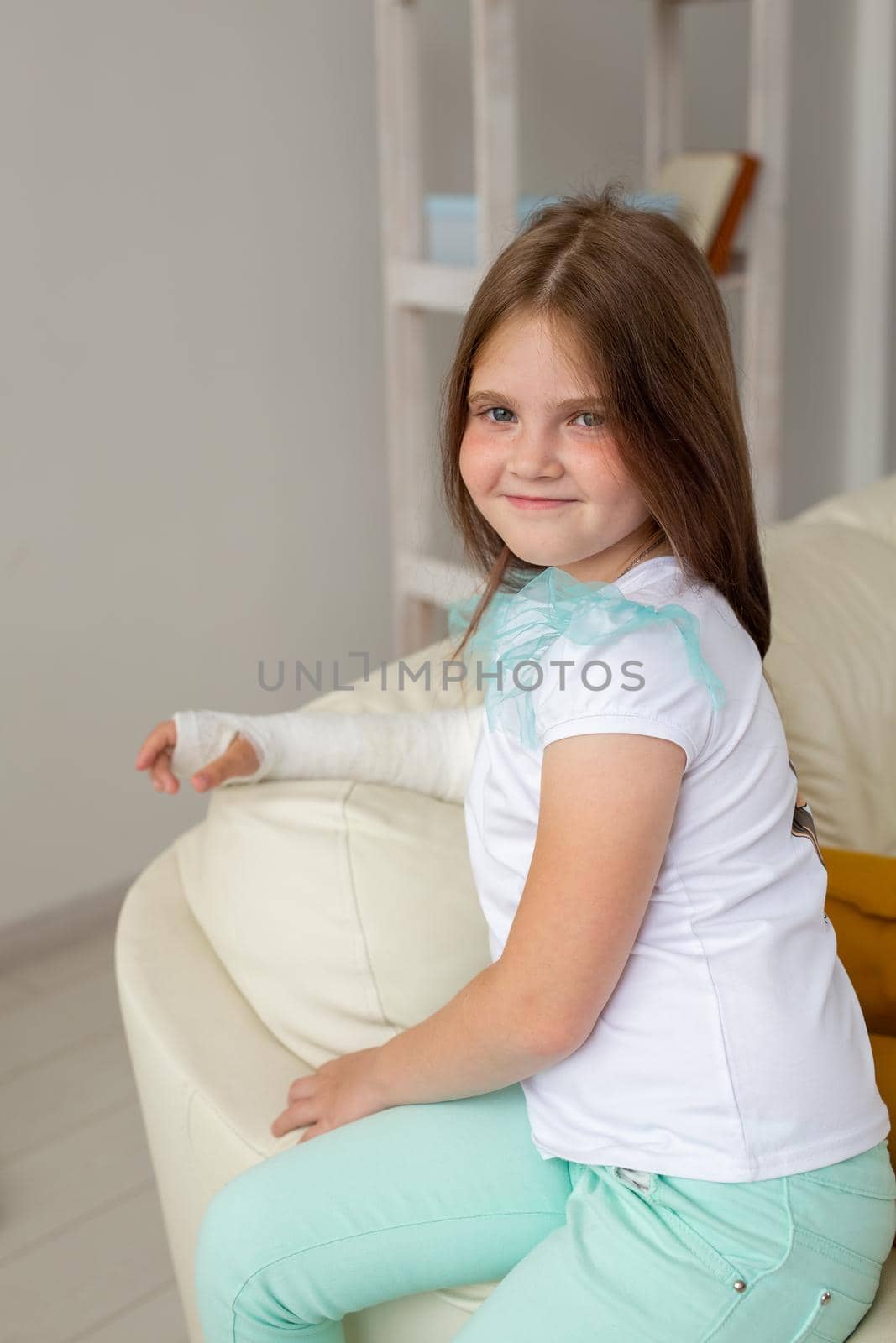 Child with a cast on a broken wrist or arm smiling and having fun on a couch. Positive attitude, recovery and kid.